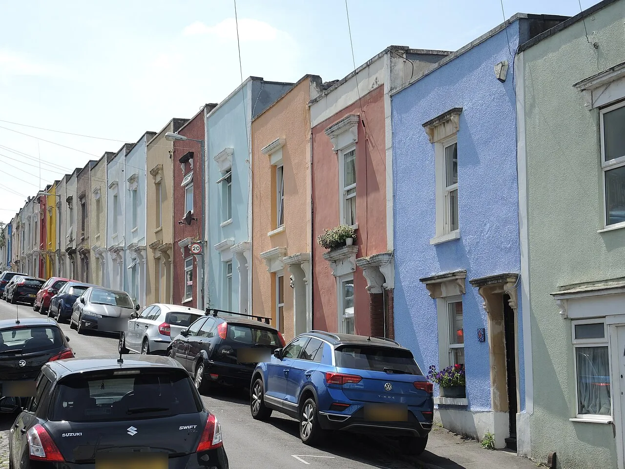 A row of colourfully painted two-storey terraced houses on Eldon Terrace, Windmill Hill, Bristol, with cars parked along the sloping street