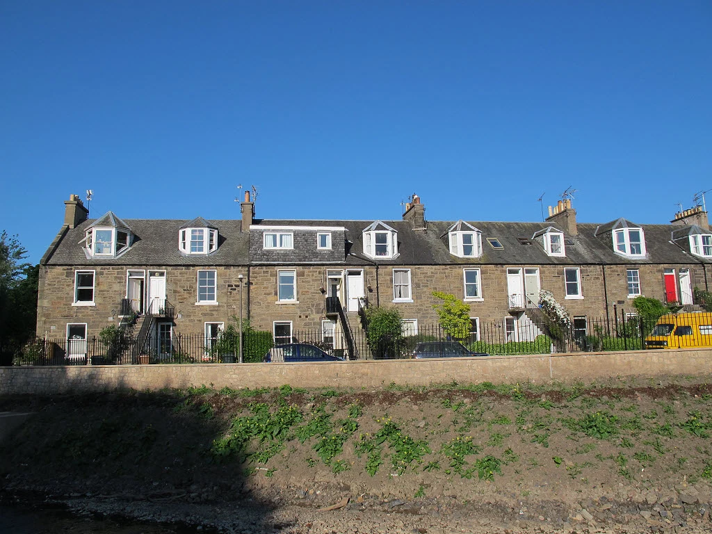 A row of two-storey stone terraced houses with dormer windows and external stairs on Reid Terrace, Stockbridge, Edinburgh, seen across the Water of Leith