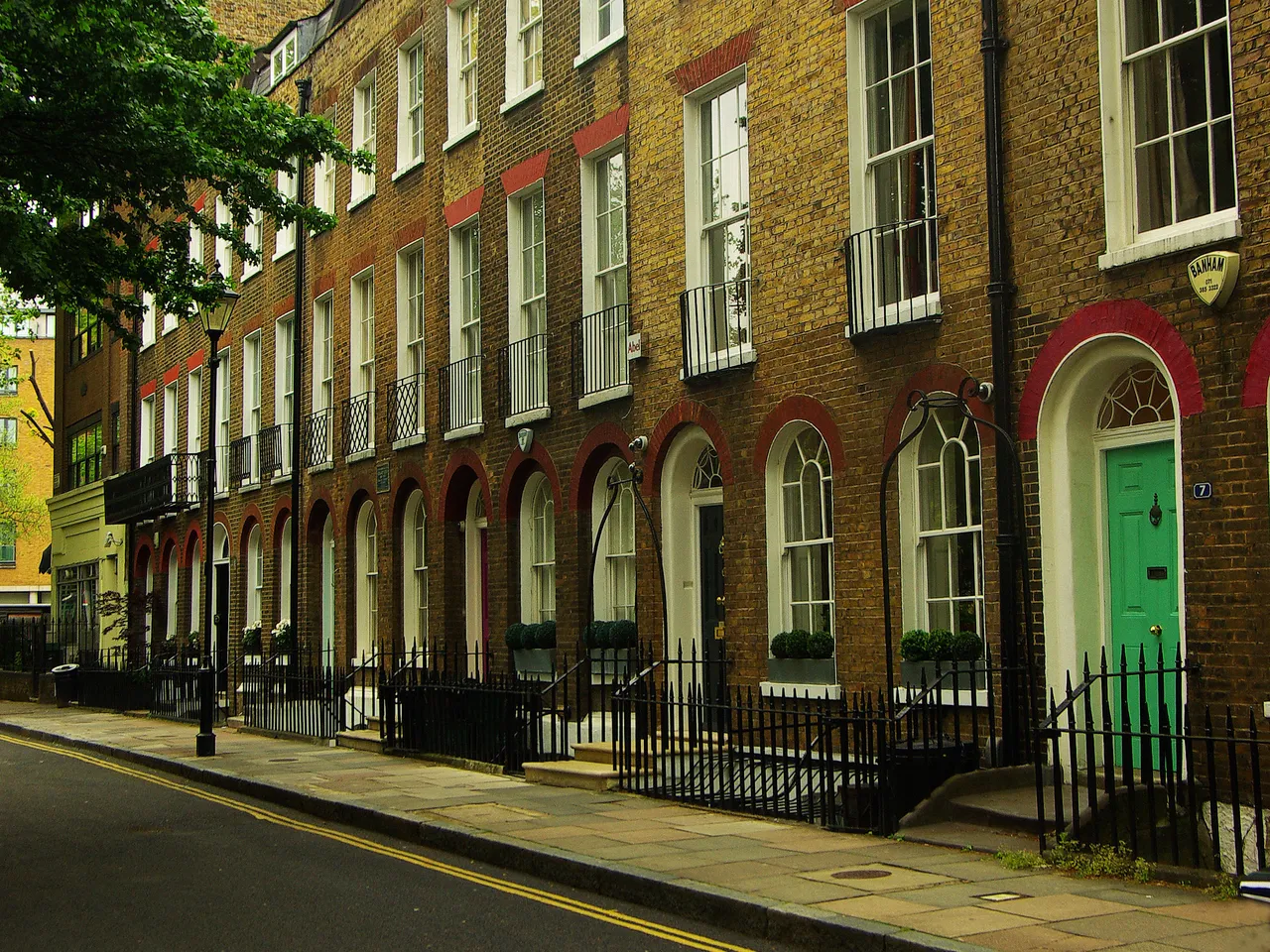 Row of brick terraced houses with sash windows, red-brick arched doorways and black railings along a quiet street on Duncan Terrace, Islington